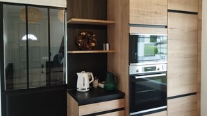 A modern kitchen with wooden cabinetry, a built-in microwave, and a kettle on the countertop. - House 300 metres from the beach (LOCTUDY)