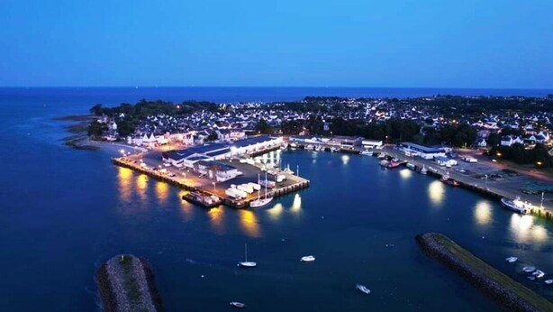 An aerial view of a coastal town at dusk with a prominent marina, residential buildings, and a large illuminated structure. - House 300 metres from the beach (LOCTUDY)
