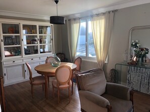 A dining area with a round wooden table, four chairs, a glass cabinet, and a window with curtains.