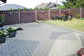 Een geplaveid terras met tuinmeubels en plantenpotten.