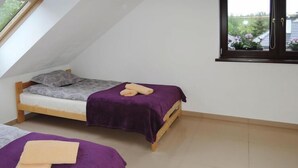 Un petit appartement d’une seule pièce, comprenant deux lits, une lucarne et une fenêtre donnant sur un espace verdoyant.