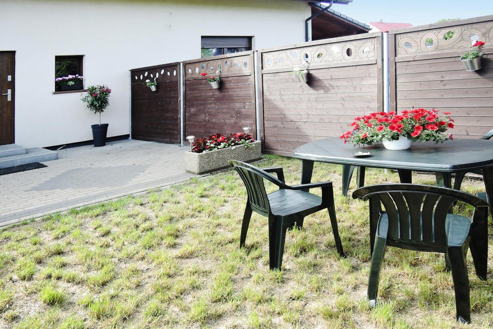 A patio area with a table and chairs, a wooden fence, and potted plants.