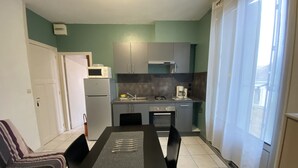 A compact kitchen with a refrigerator, microwave, and coffee maker. There is a dining table with chairs and a sofa in the adjacent living area. - **Cozy T2 in Central La Roche-Posay w/ Wi-Fi, Balcony & Close to Thermes** (La Roche-Posay)