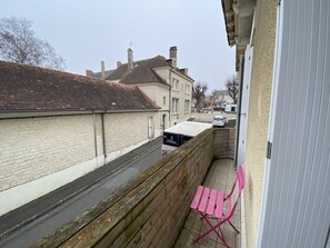 A narrow urban street with residential buildings, a parked car, and a pink folding chair on the sidewalk.
