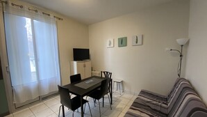 A small, well-lit room with a dining table, chairs, a sofa, a television, and a radiator. - **Cozy T2 in Central La Roche-Posay w/ Wi-Fi, Balcony & Close to Thermes** (La Roche-Posay)