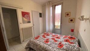 A bedroom with a bed, a radiator, a door, a window with curtains, and a wall with a picture. - **Cozy T2 in Central La Roche-Posay w/ Wi-Fi, Balcony & Close to Thermes** (La Roche-Posay)