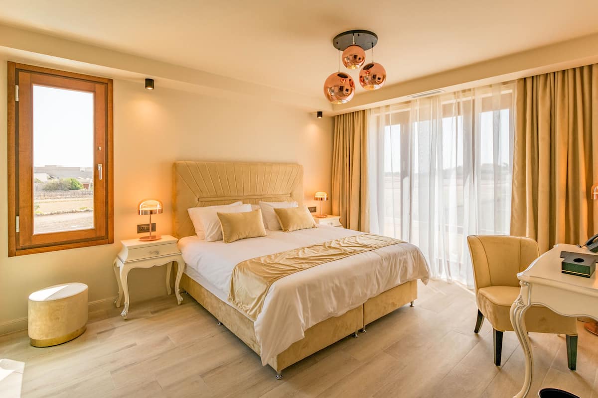 Una habitació d'hotel amb un llit gran, un escriptori, una cadira, una tauleta de nit i una finestra amb cortines.