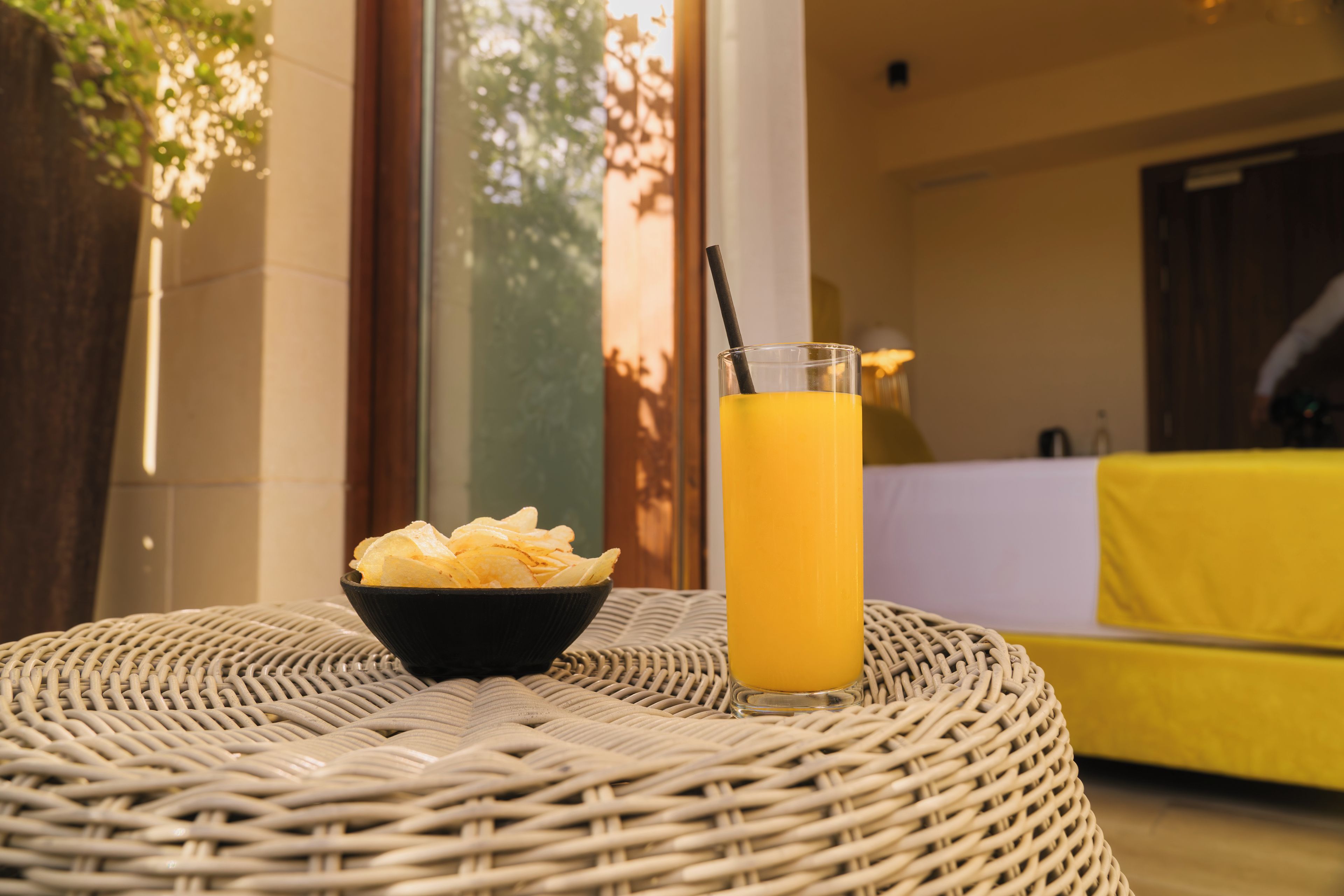 Una mesa de mimbre con un tazón de papas fritas y un vaso de jugo de naranja.