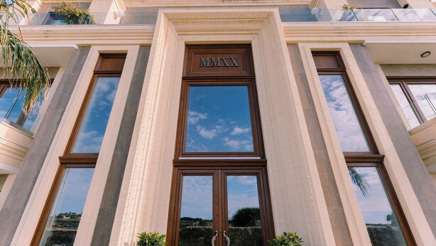 A building facade with a large central entrance, flanked by columns, and a clear sky above.