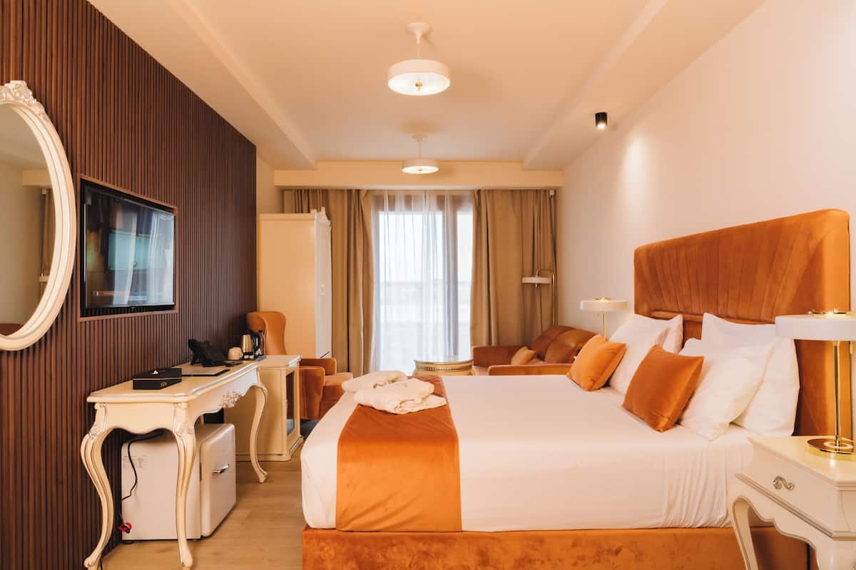 Habitació d'hotel amb un llit gran, una taula de treball, una cadira, un mirall i una televisió.