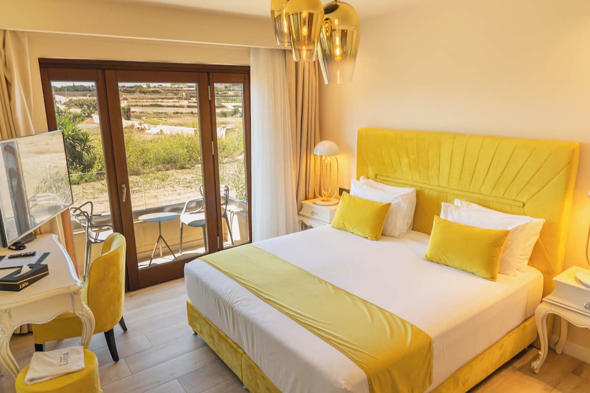 Habitació d'hotel amb un llit gran, una taula amb un ordinador, una cadira i vistes a l'exterior a través d'una porta corredissa.