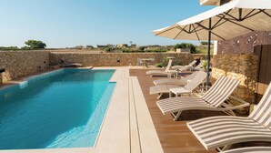 A pool area with lounge chairs and umbrellas, stone walls, and a clear view of the landscape.