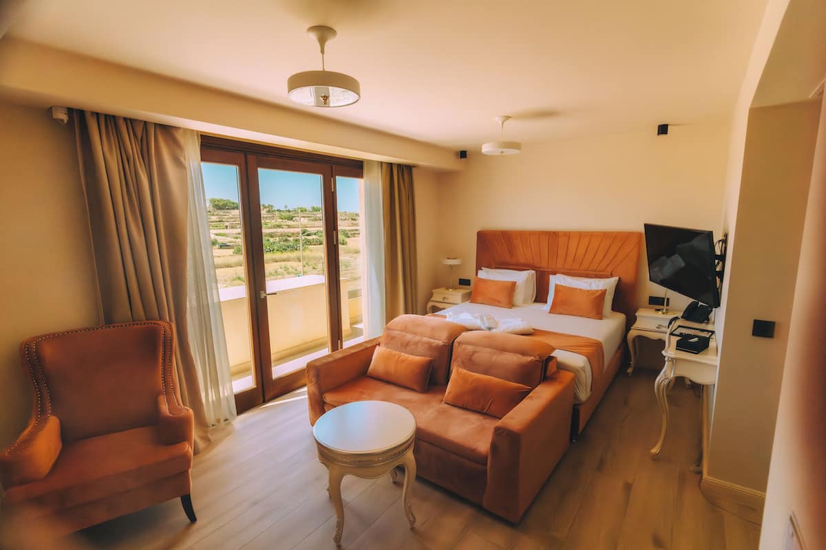 Habitació d'hotel amb llit, sofà, taula petita, escriptori amb ordinador i televisió.