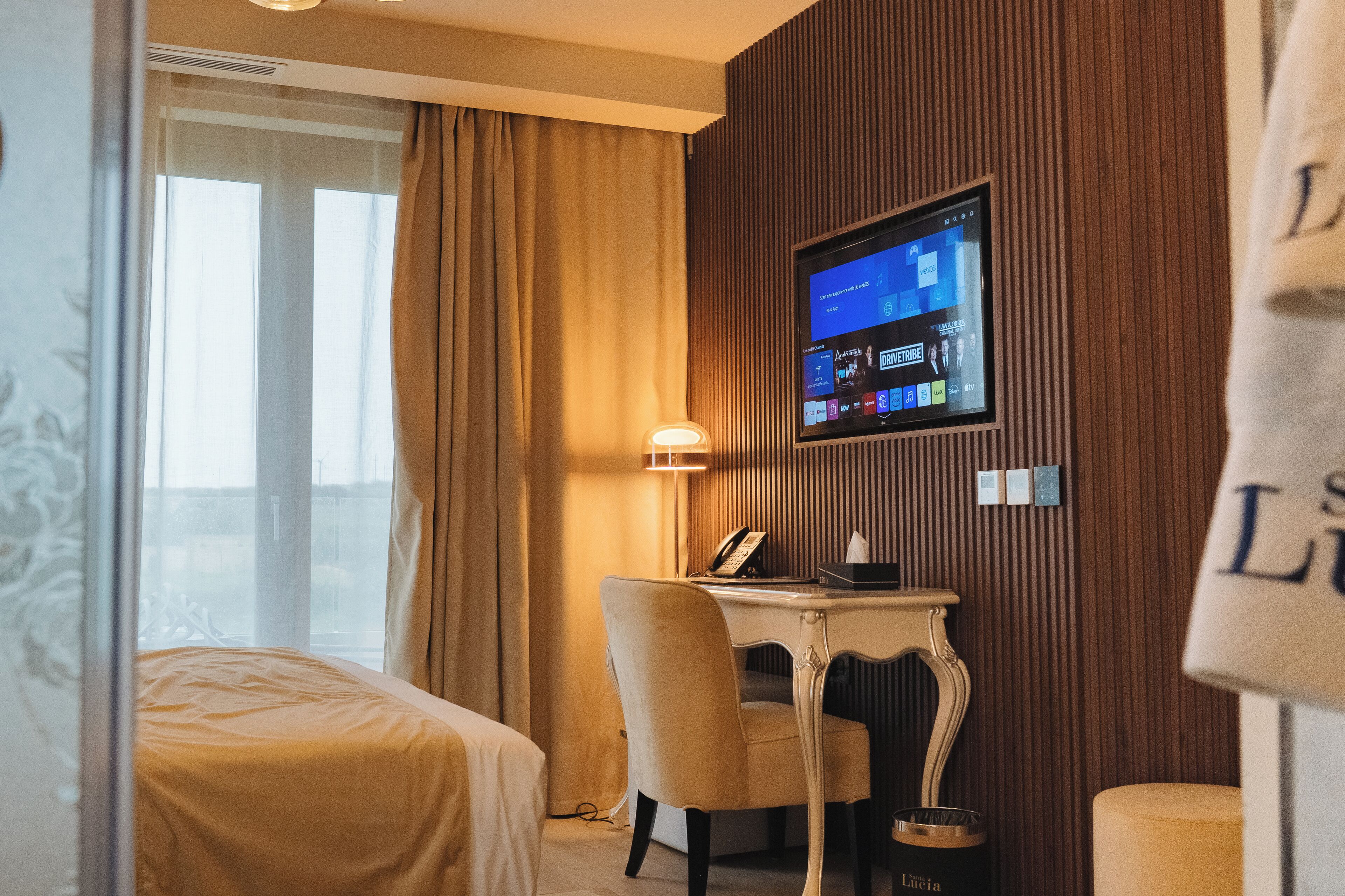 Une chambre d’hôtel équipée d’un lit, d’un bureau avec un écran d’ordinateur, d’un téléphone et d’un mini-bar.