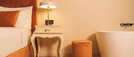 A bedroom with a bed, nightstand, lamp, and a bathtub.