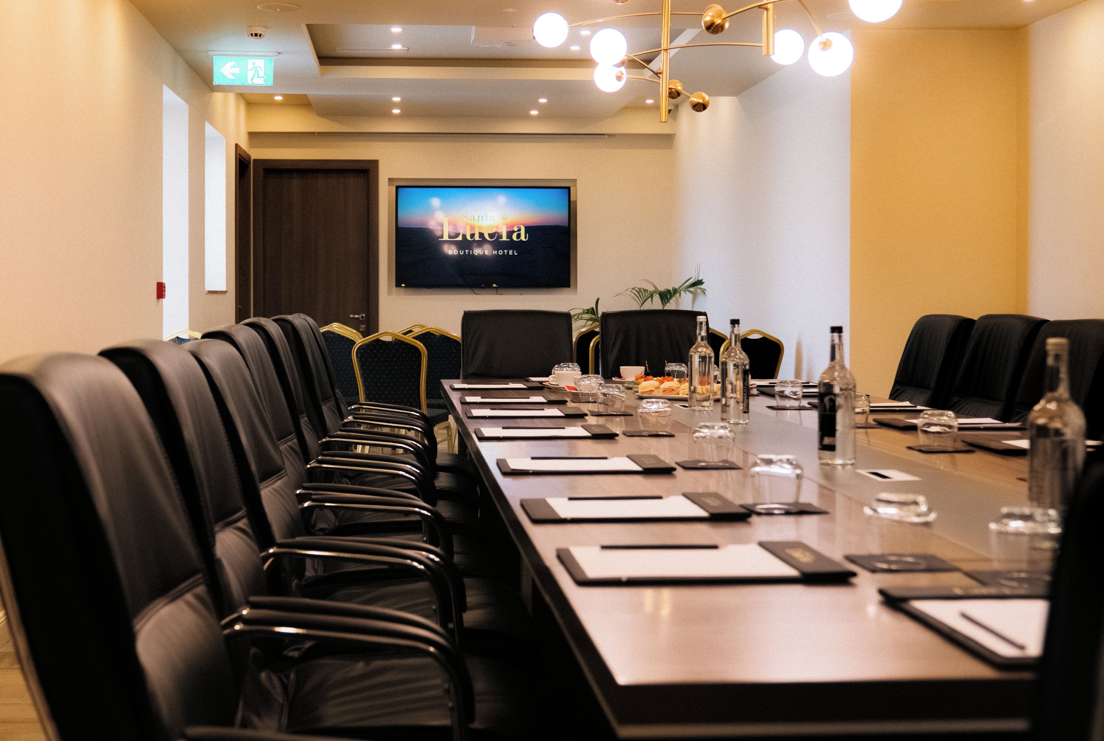 A conference room with a long table, chairs, and a television screen displaying 'Santa Lucia Boutique Hotel'.