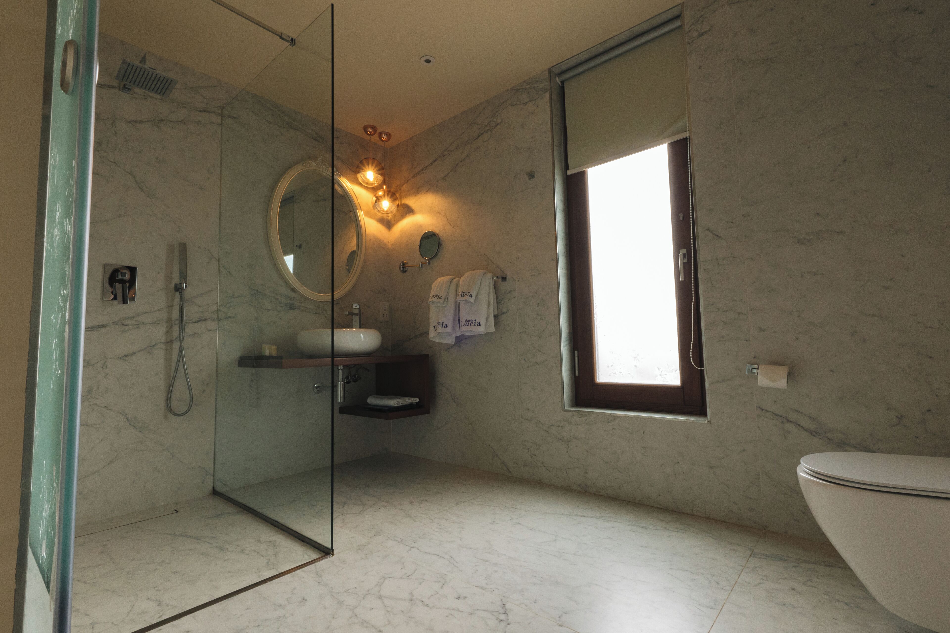 Une salle de bain moderne avec une douche à parois de verre, un miroir rond, des toilettes et un lavabo.
