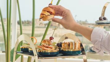 A hand holding a sandwich with a toothpick, with a buffet table in the background.