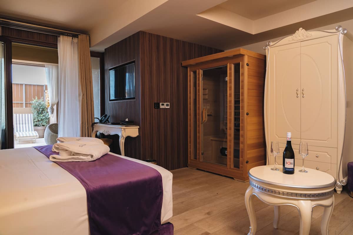 Una habitació d'hotel amb un llit, una taula de nit, un armari i una taula petita amb una ampolla i vasos.