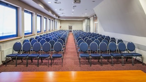 A conference room with rows of blue chairs, a projector, and large windows. - Hotel Festival (Opole)