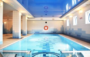 An indoor swimming pool with a blue and white tiled floor, a central lifebuoy, and a ceiling with a blue pattern. - Hotel Festival (Opole)
