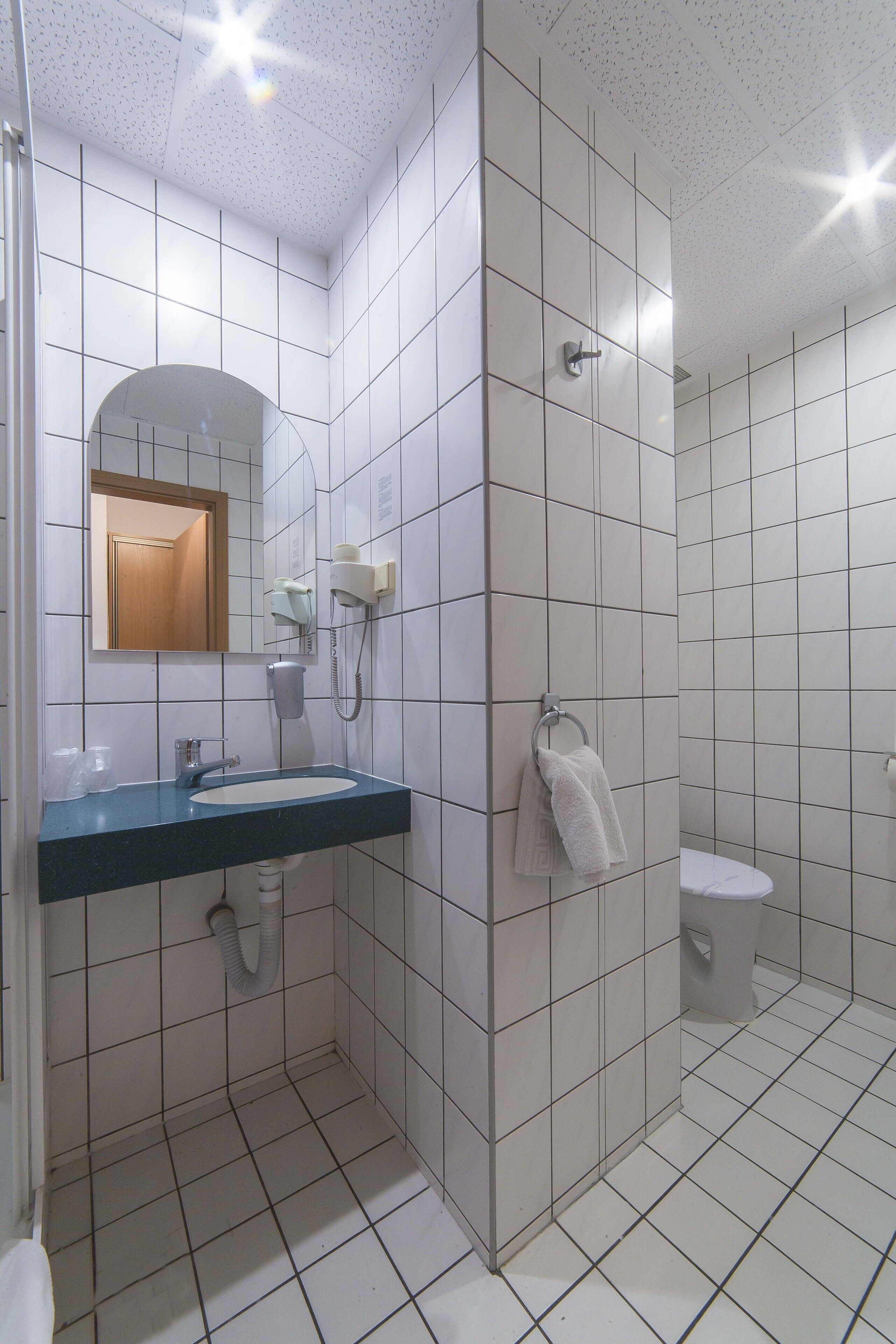 A bathroom with white tiled walls, a blue sink, a mirror, a towel rack, a toilet, and a shower area.