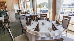 A restaurant with round tables, chairs, and a view of the street through large windows. - Hotel Festival (Opole)