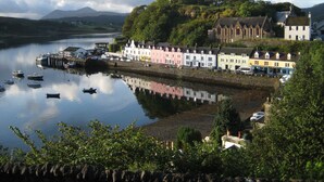 A coastal town with colorful buildings along the waterfront, boats docked at the pier, and a mountain in the background. - Kinloch Ainort Apartments  (Sconser)