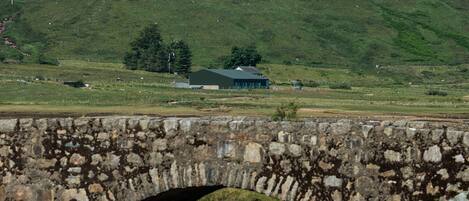 A stone bridge over a river with a green landscape and a building in the background.