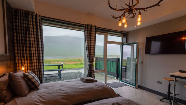 A bedroom with a large bed, a television, and a view of a lake and mountains. - Kinloch Ainort Apartments  (Sconser)
