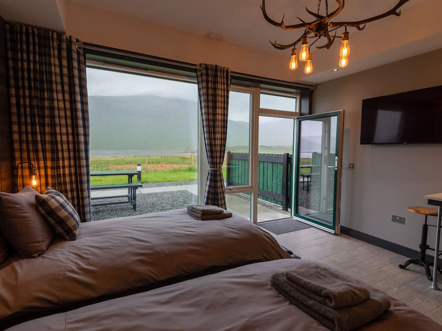 A bedroom with a large bed, a television, and a view of a lake and mountains.