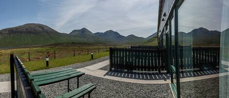 A view from a building's balcony overlooking a grassy field with mountains in the distance.
