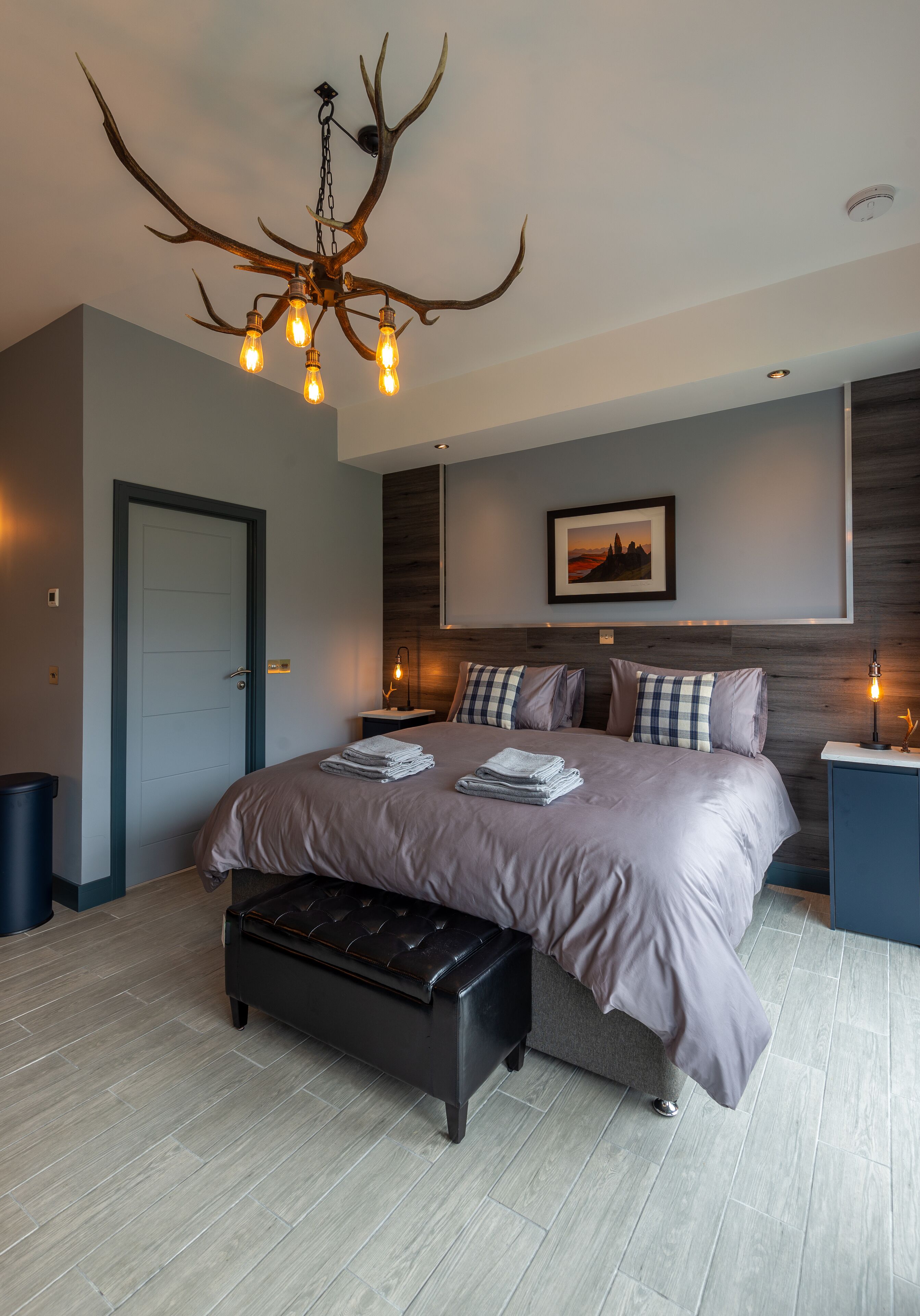 A modern bedroom with a large bed, a unique antler chandelier, and a framed picture on the wall.