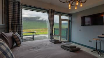 A bedroom with a large bed, plaid curtains, a television, and a view of a green landscape.