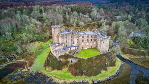 A castle with multiple towers, surrounded by a moat and lush greenery. - Kinloch Ainort Apartments  (Sconser)
