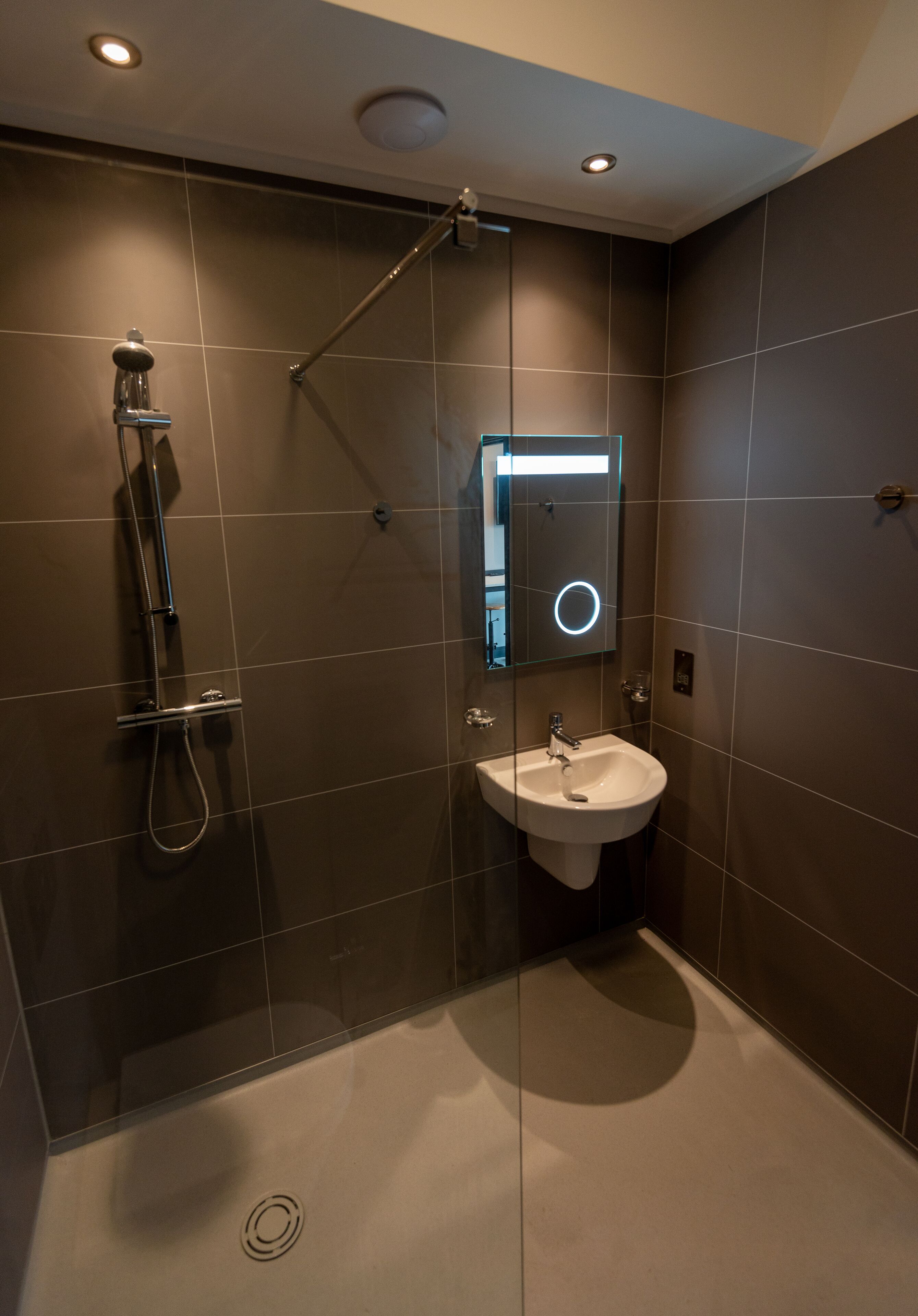 Un bagno moderno con cabina doccia in vetro, un lavandino bianco e uno specchio con illuminazione circolare.