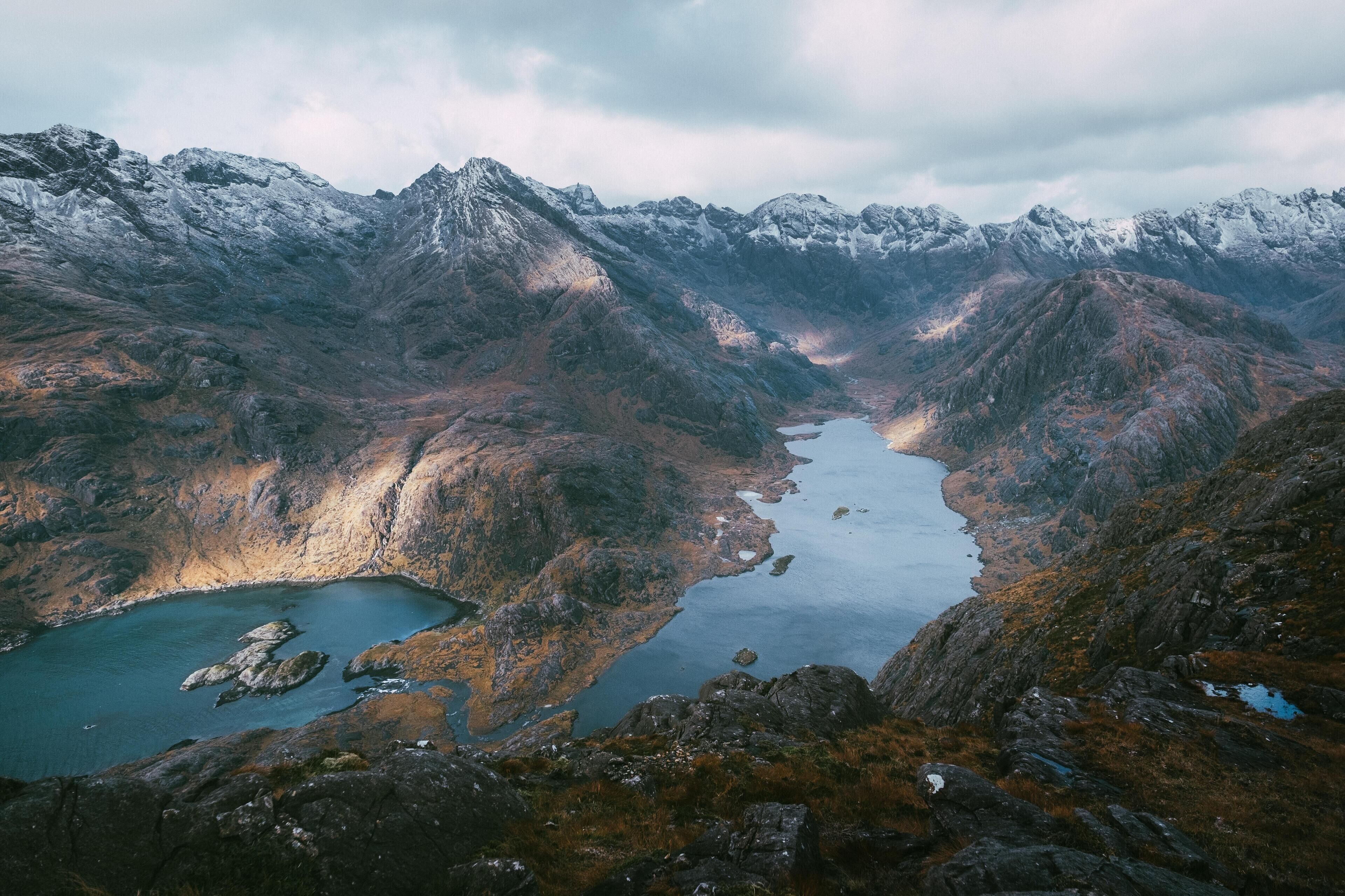 A mountainous landscape with a lake surrounded by rocky terrain and snow-capped peaks.