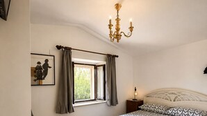 A bedroom with a bed, a window with curtains, a chandelier, and a framed picture on the wall. - Tuscan House in the Green (Toscana)