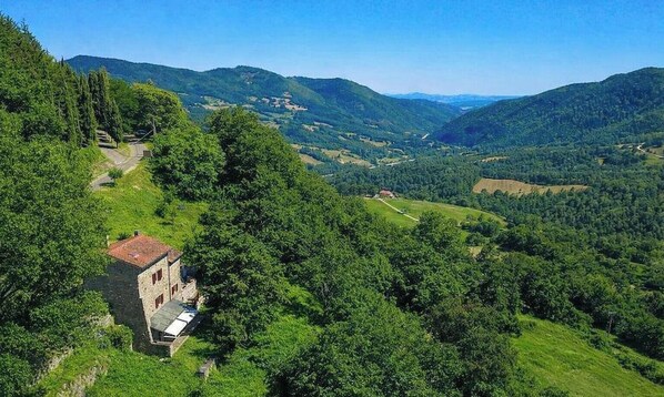 A rural landscape with a stone building, surrounded by lush greenery and rolling hills.