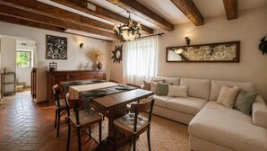 A dining area with a wooden table and chairs, a sofa, and a chandelier. - Tuscan House in the Green (Toscana)