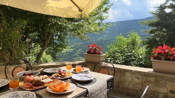 An outdoor dining area with a table set for breakfast, surrounded by lush greenery and a scenic mountain view. - Tuscan House in the Green (Toscana)