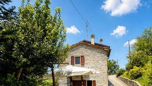 A stone house with a gravel driveway, a wooden fence, and potted plants. - Tuscan House in the Green (Toscana)