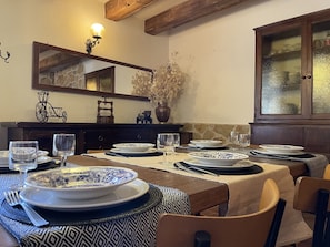 A dining area with a wooden table set for four, surrounded by chairs. A mirror hangs above the table, and a cabinet with glass doors is to the right.