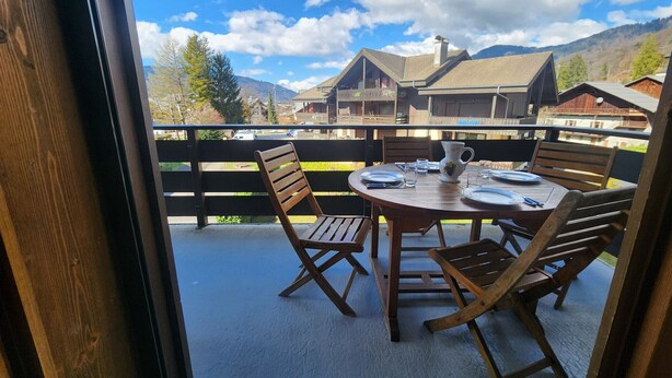 A wooden table set for four on a balcony with a view of houses and mountains. - Cozy 4-person apartment with balcony & garage in Samoëns (Samoëns)