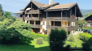 A two-story chalet with a balcony, surrounded by lush greenery and mountains in the background. - Cozy 4-person apartment with balcony & garage in Samoëns (Samoëns)