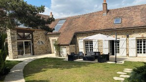 A stone building with a tiled roof, a covered patio with outdoor furniture, and a stone pathway leading to the entrance.