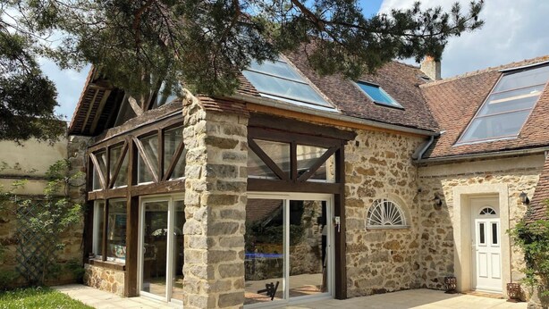 A stone building with a glass conservatory, wooden beams, and a tiled roof.