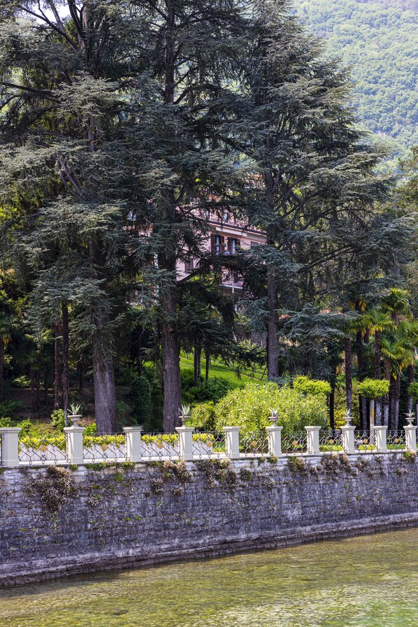 A serene riverside setting with a stone wall, lush greenery, and a building in the background.