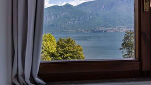 Uitzicht vanuit een raam met gordijnen, op een meer en bergen.
