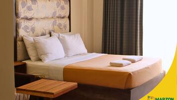 A hotel room with a bed, pillows, a wooden nightstand, and a table.